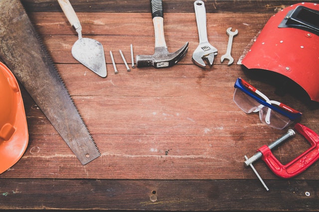 ​​An array of tools laid out on a table including a saw, hammer, wrench, and welding mask